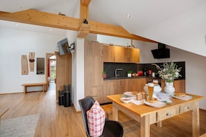A modern kitchen with wooden cabinets, a dining table with plates, and a bench in a bright room with wooden beams.