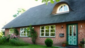 Une maison en briques avec un toit de chaume, une porte verte et un petit jardin fleuri.