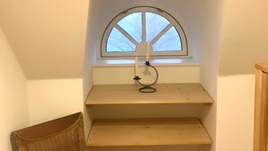 Une pièce avec un plafond en pente, une fenêtre surmontée d’une arche et une chaise en bois.
