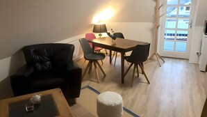 Un coin repas comprenant une table, des chaises, une lampe et une vue sur l’extérieur, visible à travers une porte.