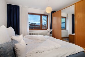 Un dormitorio con una cama grande, un armario de madera, un ventanal con vistas y un radiador.