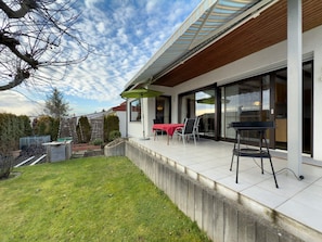 Ein modernes Haus mit Terrasse, einem roten Tisch und einem Grill.