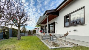 Een modern huis met een terras, een vogelhuisje en een tuin.