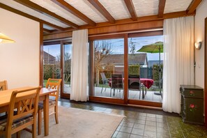 Un comedor con una mesa y sillas de madera, un amplio ventanal corredero que da a un patio exterior y un mueble bajo con diseño floral.