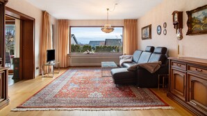 Een woonkamer met een groot raam, een kroonluchter, een bank, een televisie en een open haard.