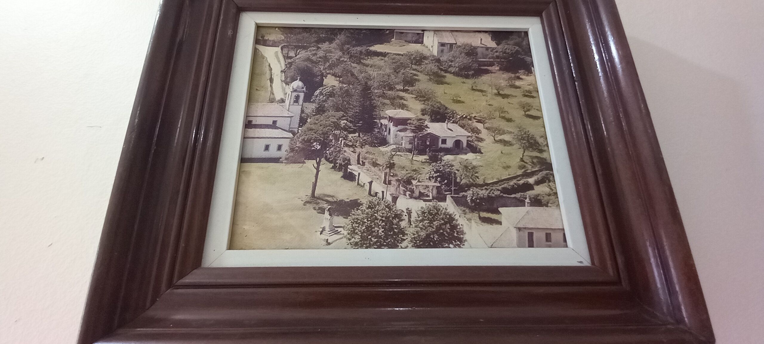 A framed black and white photograph of a town with buildings, trees, and a church.