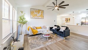 A modern living room with a white sofa, a black sofa, and a coffee table. There is a ceiling fan and a painting on the wall. - Tranquil 3-bedroom house in Austin with WiFi and AC (Austin)