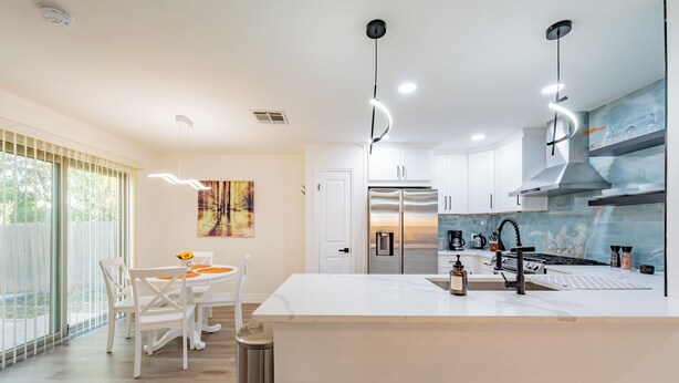A modern kitchen with white cabinetry, a stainless steel refrigerator, and a large island with a sink. - Tranquil 3-bedroom house in Austin with WiFi and AC (Austin)