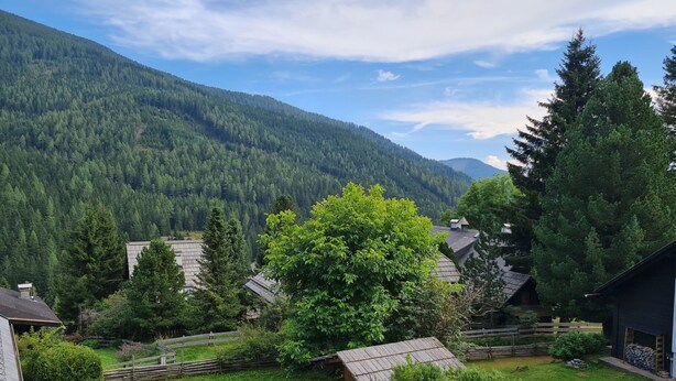 Uma aldeia rural com casas rodeadas por vegetação exuberante e montanhas ao fundo.
