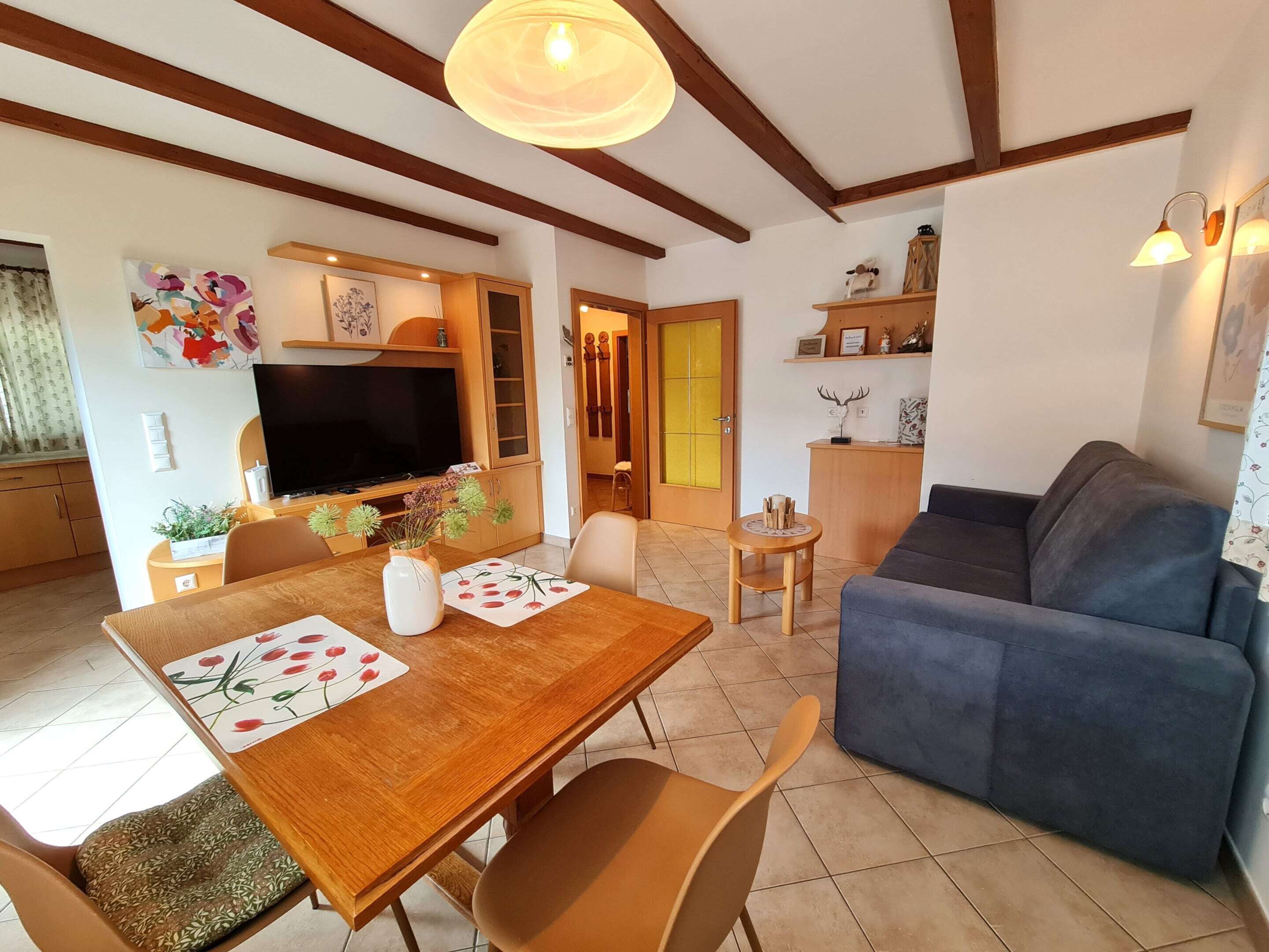 A living room with a sofa, a dining table with chairs, a TV, and a kitchen area with cabinets.