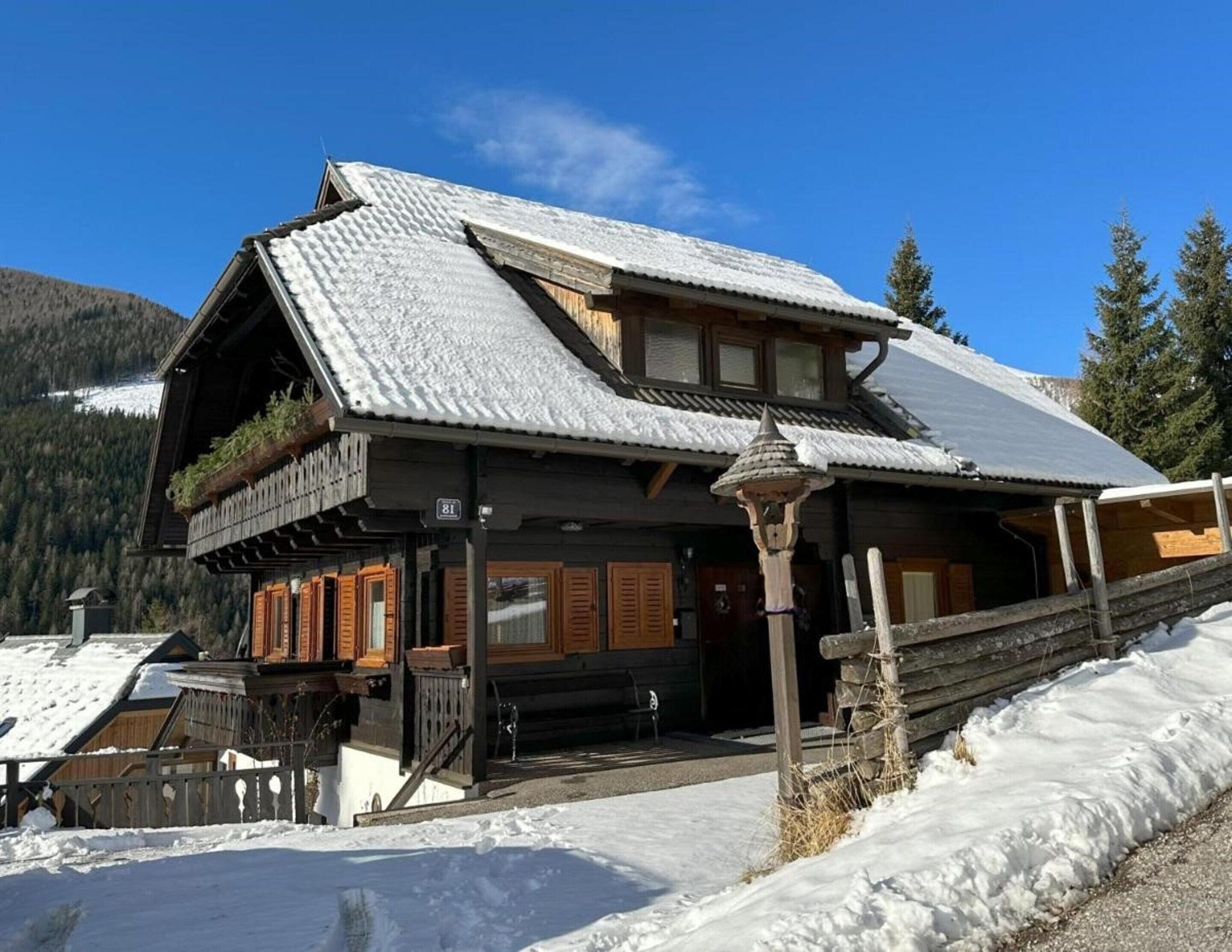 A wooden chalet with a sloped roof, wooden shutters, and a balcony with plants.