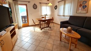Uma sala de estar com sofá, uma mesa de jantar com cadeiras, uma televisão e um relógio na parede.