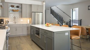 Een moderne keuken met grijze kastjes, een roestvrijstalen koelkast en een centraal eiland met stoelen.