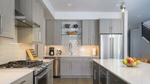 Een moderne keuken met grijze kastjes, roestvrijstalen apparatuur en een centraal kookeiland met fruit.