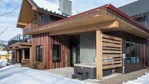 Een modern houten huis met een overdekte veranda, grote ramen en een zichtbare terrasverwarmer.