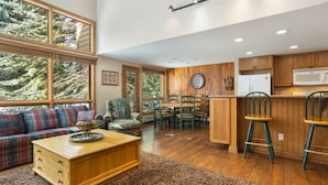 A spacious living area with a sofa, a wooden coffee table, and a dining table with chairs. There is a kitchen area with wooden cabinets and a microwave. - East Vail Townhome - Close to Racquet Club (Vail)