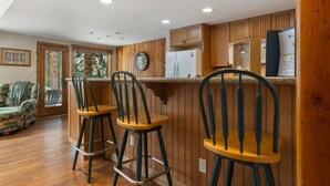 A kitchen with wooden paneling, a refrigerator, a clock, and two bar stools. - East Vail Townhome - Close to Racquet Club (Vail)