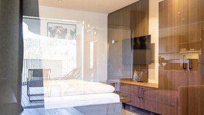 A modern bedroom with a large bed, a TV mounted on a wooden cabinet, and a balcony with outdoor furniture.
