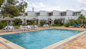 Une piscine entourée de chaises longues et de parasols, le tout bordé d’un bâtiment doté de balcons et d’un jardin.