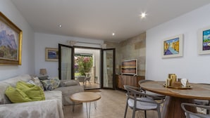 Un salon comprenant un canapé, une table basse et un coin repas avec des chaises et une table. Les murs sont ornés de tableaux et il y a une fenêtre avec vue.