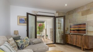 Un salon comprenant un canapé, un téléviseur posé sur un meuble en bois et une porte vitrée donnant sur un espace extérieur avec une table et des chaises.
