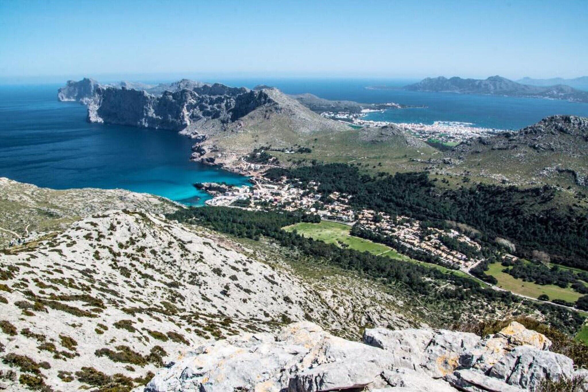 A mountainous landscape with a coastal town, rocky terrain, and clear blue waters.