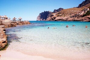 A beach with clear water, rocky terrain, and a few umbrellas. - House in Pollensa near Cala Barqués Beach (Pollensa)