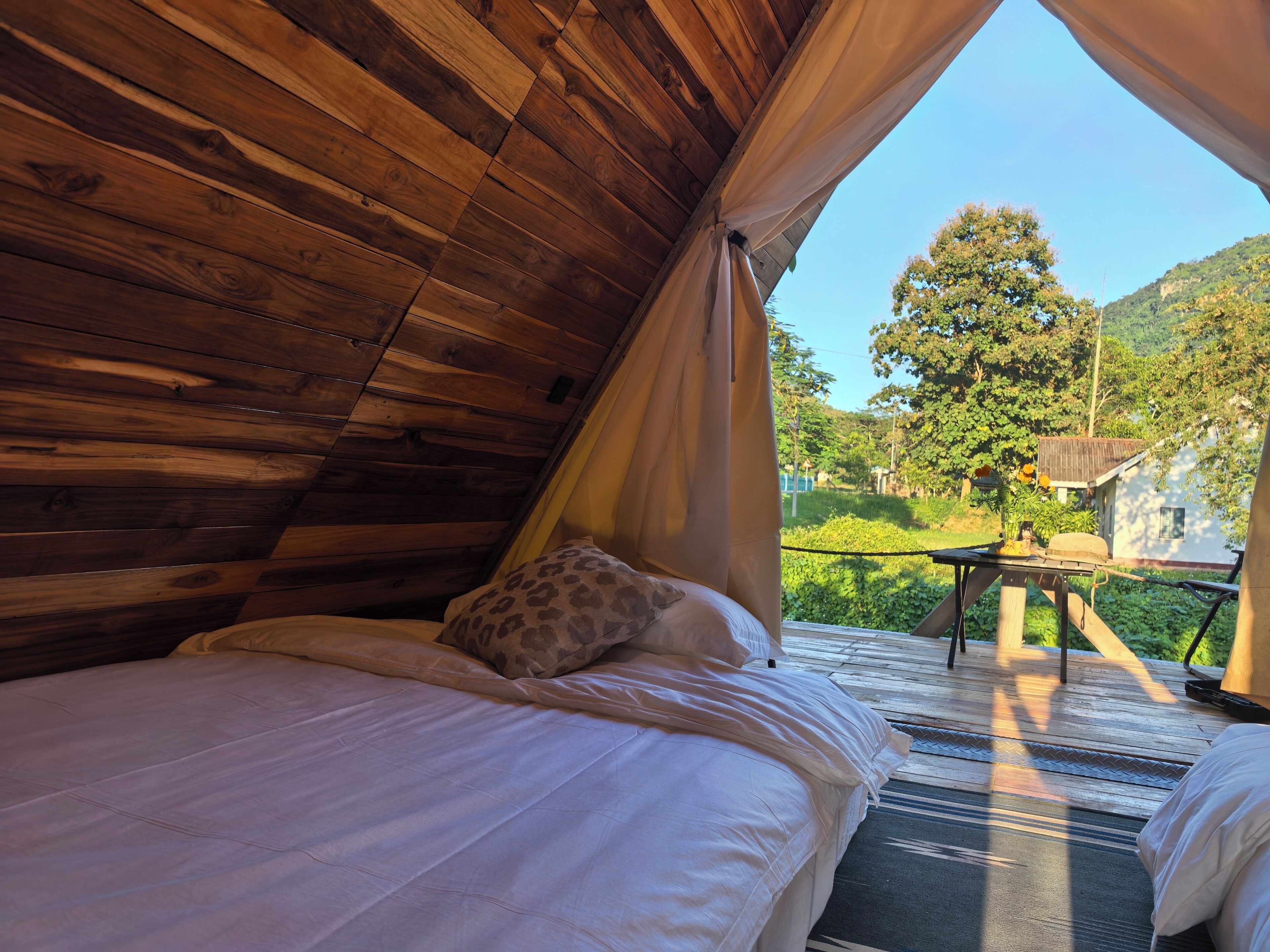Una habitación acogedora de madera con dos camas, una mesa y vistas a un exuberante jardín y colinas.
