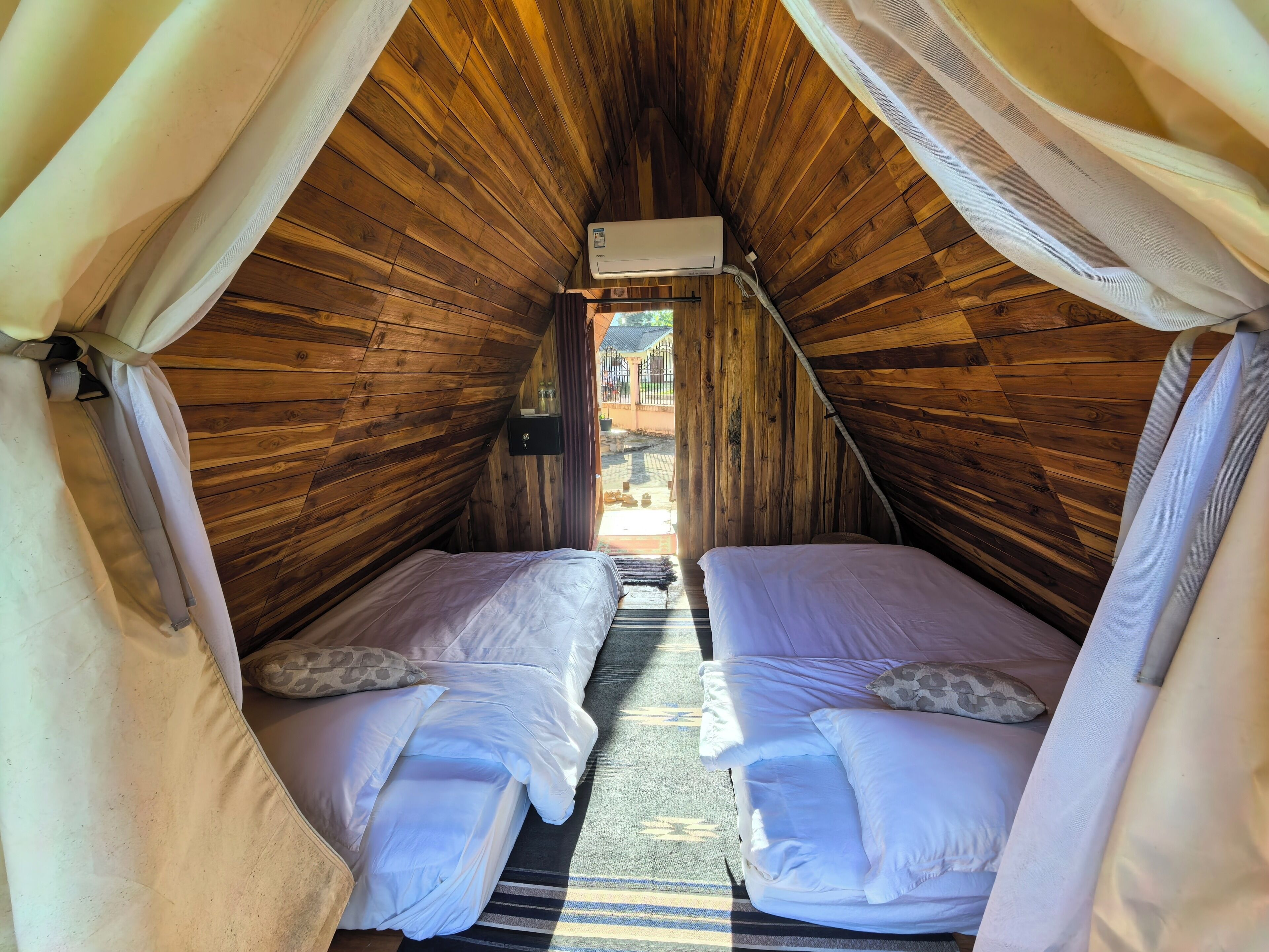 Un acogedor dormitorio en ático con paredes de madera, dos camas, un ventilador de techo y una ventana.