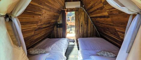 Un acogedor dormitorio en ático con paredes de madera, dos camas, un ventilador de techo y una ventana.