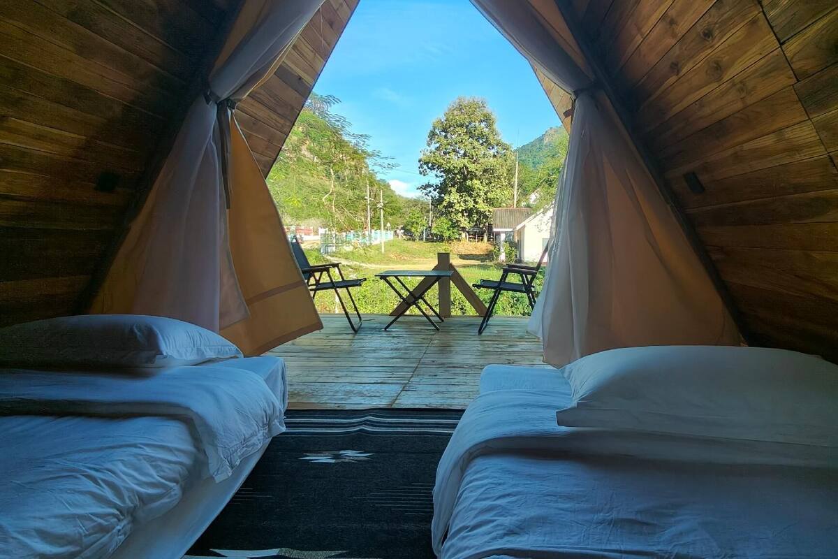 A tented accommodation with two beds, a picnic table, and a view of the surrounding landscape.