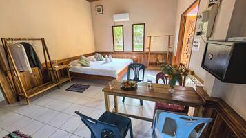 A room with a bed, a wooden bench, a table with chairs, a small rug, and a wall-mounted TV.
