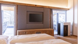 A bedroom with a large bed, a television mounted on a wooden panel, and a sliding glass door leading to a balcony. - Lush Apartment in Tyrol With Sauna (Lermoos)