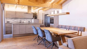 A modern kitchen with wooden beams, a central island, grey chairs, and a wooden dining table. - Lush Apartment in Tyrol With Sauna (Lermoos)