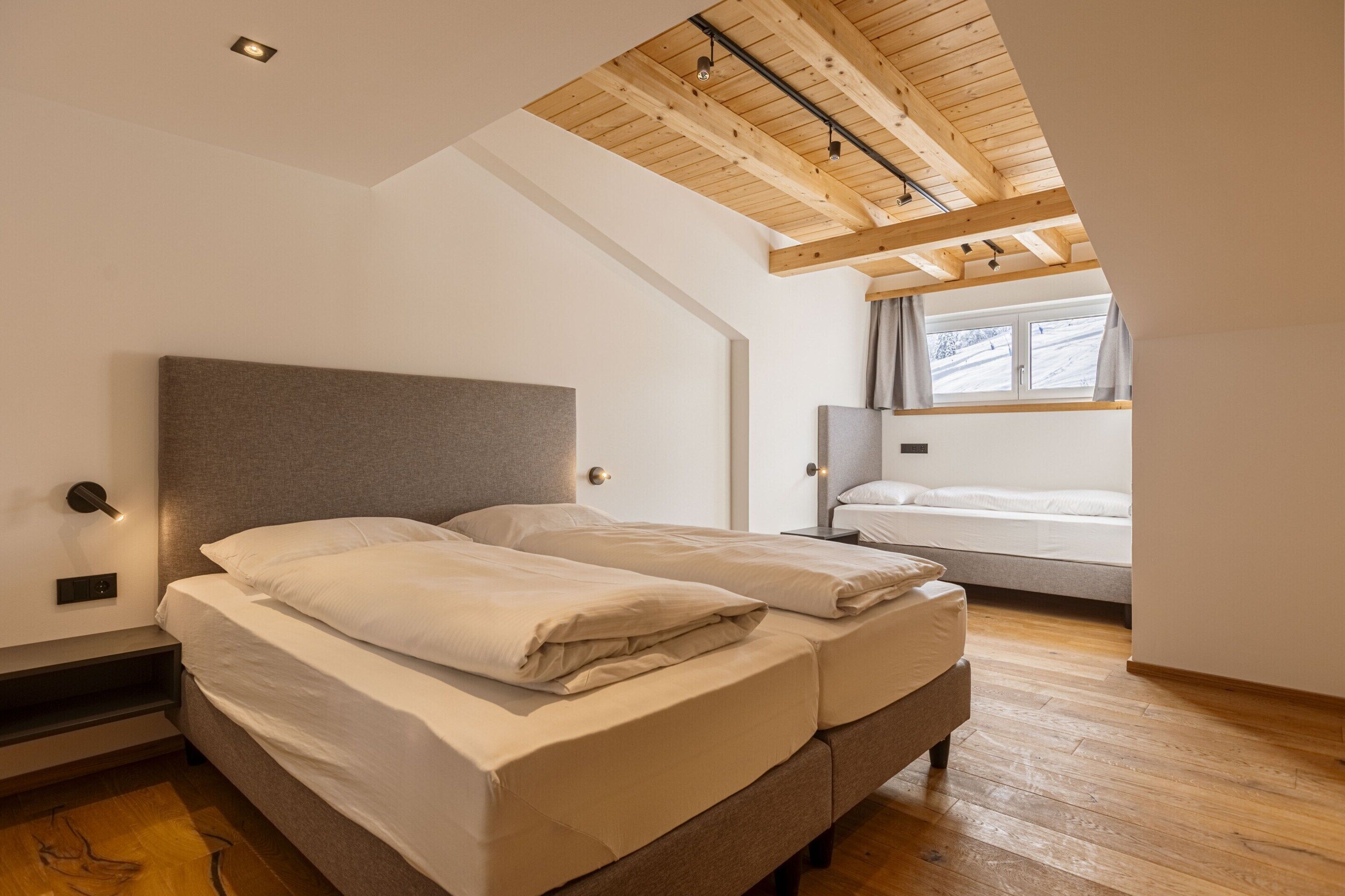 A bedroom with a wooden ceiling, a bed with white bedding, a bedside table, and a window with curtains.