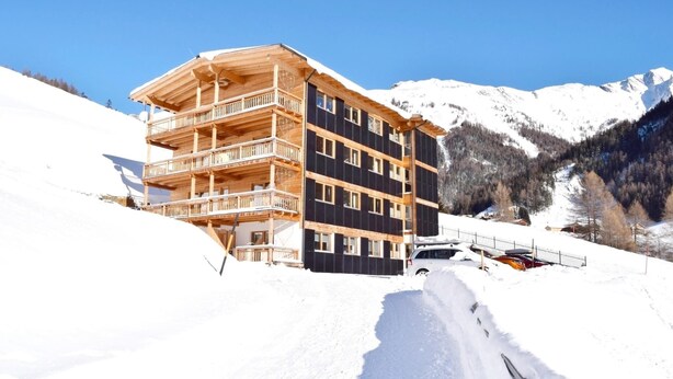 A multi-story wooden building with balconies, surrounded by snow-covered mountains.