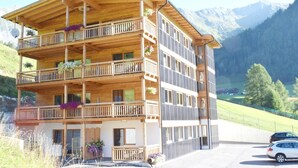 A multi-story wooden chalet with balconies, surrounded by mountains.