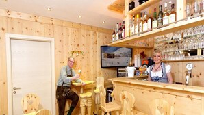 A bar area with wooden furniture, shelves with bottles and glasses, and a television displaying a snowy scene.