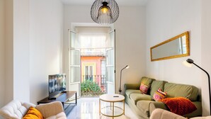 Una sala de estar moderna con sofá, sillones, una mesa de centro, televisor y un balcón con barandilla.