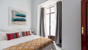 Un dormitorio con cama, ventana con cortinas, puerta y una obra de arte colgada en la pared.
