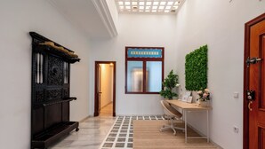 Un pasillo con un banco de madera, un escritorio con una planta y una puerta decorada con un adorno verde en la pared.