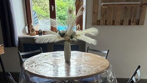 A round dining table with a clear plastic cover, surrounded by metal chairs with blue cushions. - On grassland (Malmerspach)