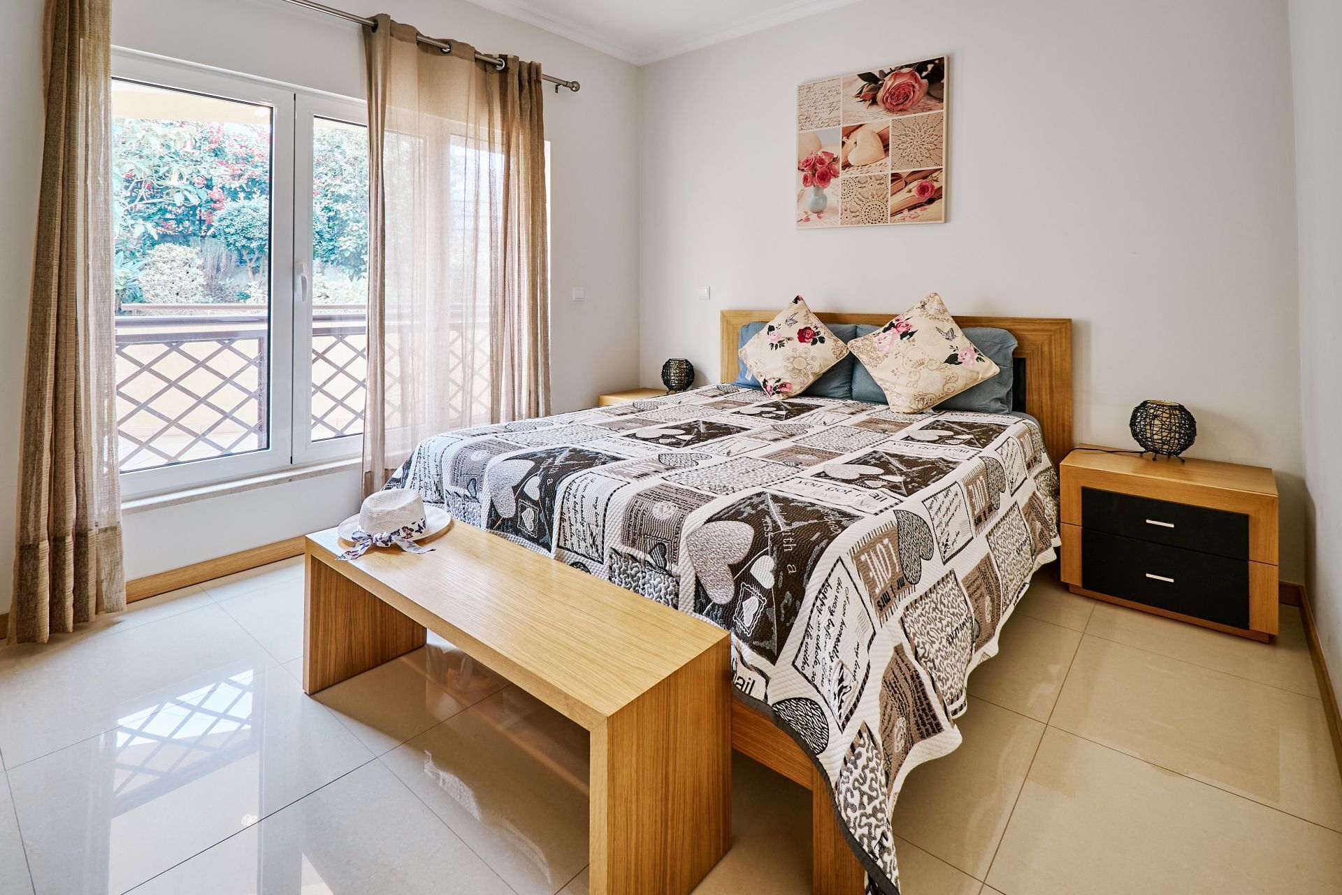 A neatly arranged bedroom with a large bed, a bedside table, a nightstand, and a window with curtains.