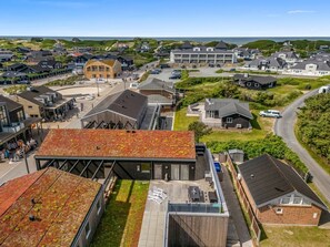 A coastal residential area with modern houses, a large building with a flat roof, and a view of the sea.