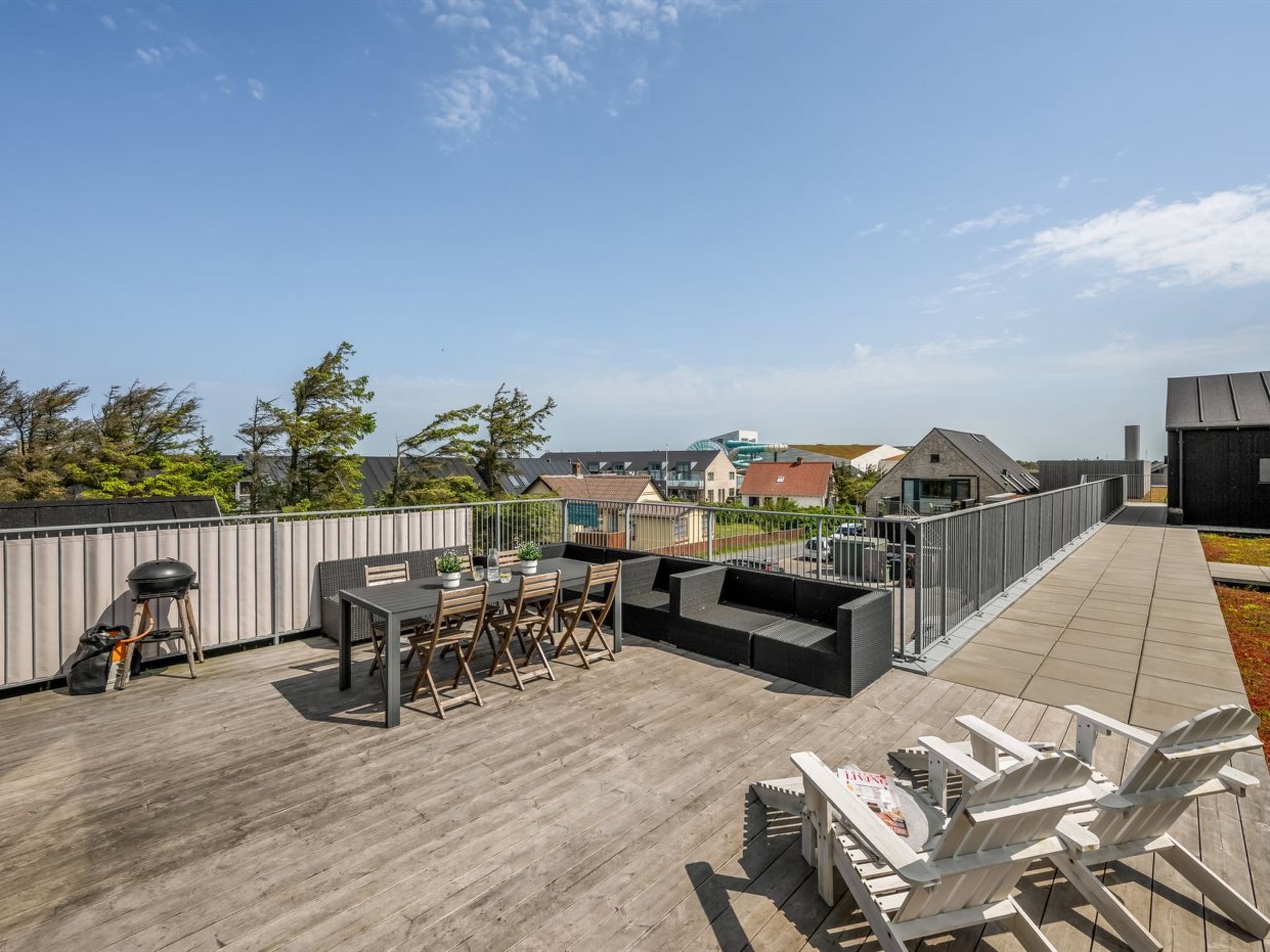 Eine Dachterrasse mit Tisch und Stühlen, einem Grill und Adirondack-Sesseln.