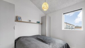 Ein Schlafzimmer mit Bett, einem Fenster mit Blick, einer Pendelleuchte und einem Regal mit Gegenständen.