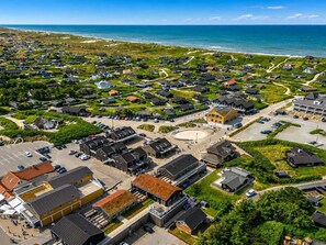 An aerial view of a coastal residential area with houses, a central circular plaza, and a parking lot.