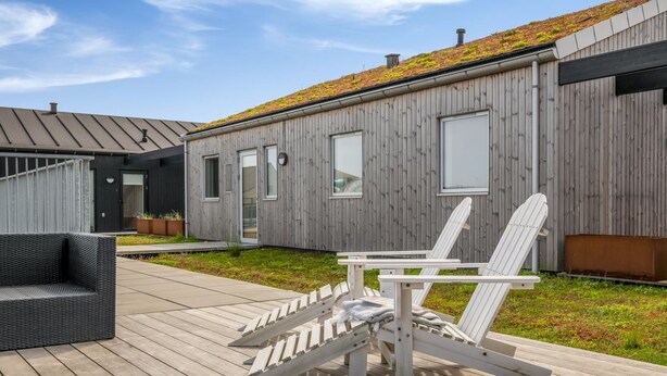 Ein modernes Gebäude mit Holzfassade, einem begrünten Dach und einer Terrasse mit Gartenmöbeln.