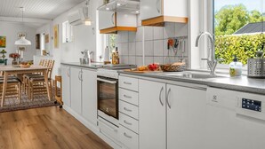 Eine moderne Küche mit weißen Schränken, einem eingebauten Backofen und einem großen Fenster mit Blick ins Freie.