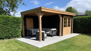 A covered outdoor seating area with a wooden structure, a sofa, and two chairs. - Lovely Bungalow With Garden (Breskens)